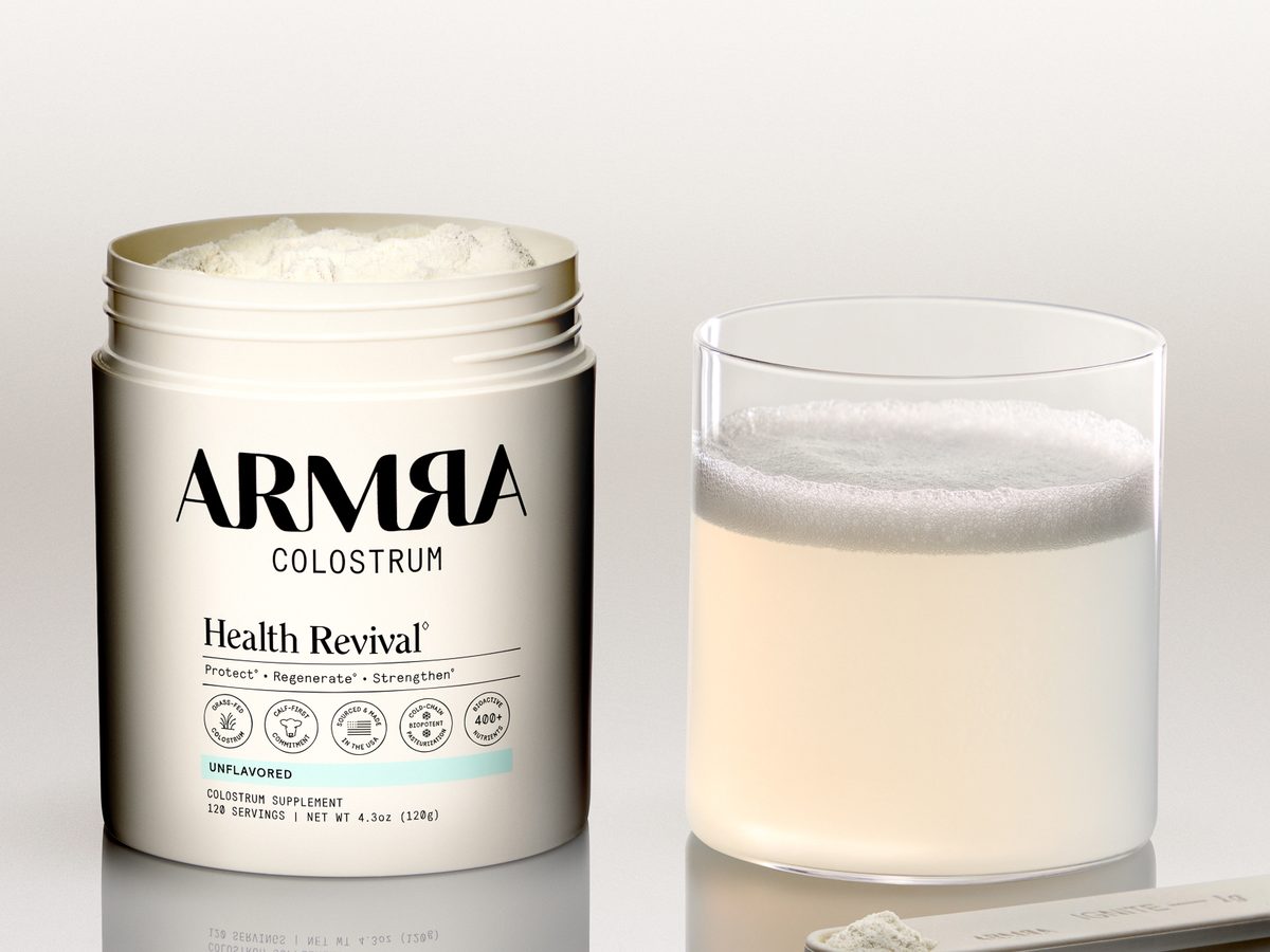 ARMRA Colostrum unflavored jar, lid off, beside a glass of the mixed drink