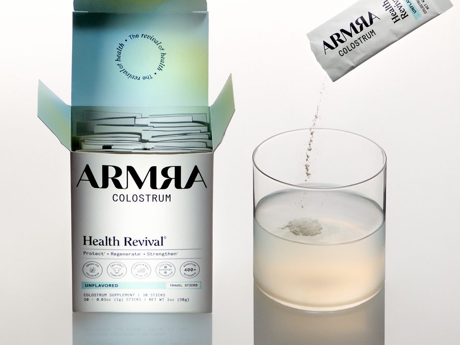 ARMRA Colostrum single-serve travel stick being poured into a glass of water beside its box